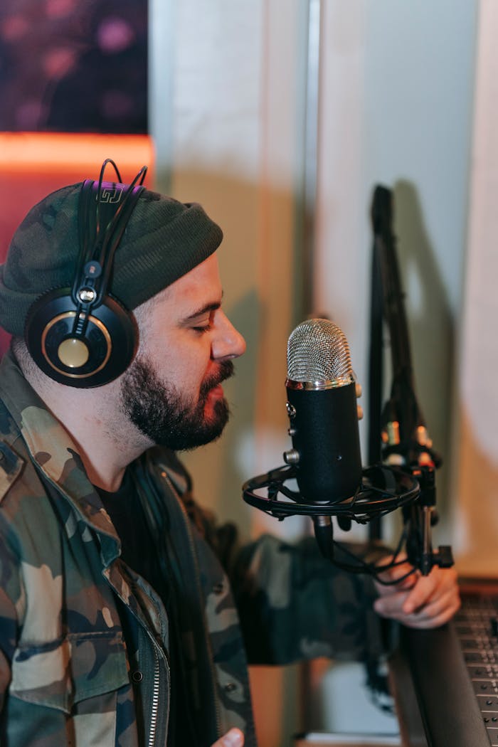 gallery-5 Man in headphones singing into a microphone in a home studio setting.