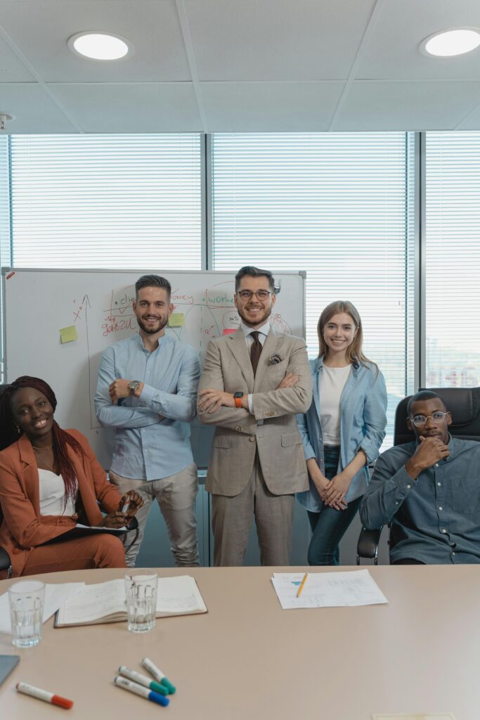 pexels photo 5439475 5439475 Five coworkers smiling and posing in a bright modern office with a whiteboard and window view.