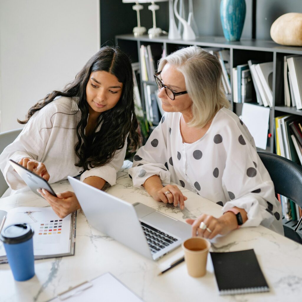 pexels photo 8837787 8837787 Two professional women discussing work on a laptop and tablet in a contemporary office setting.